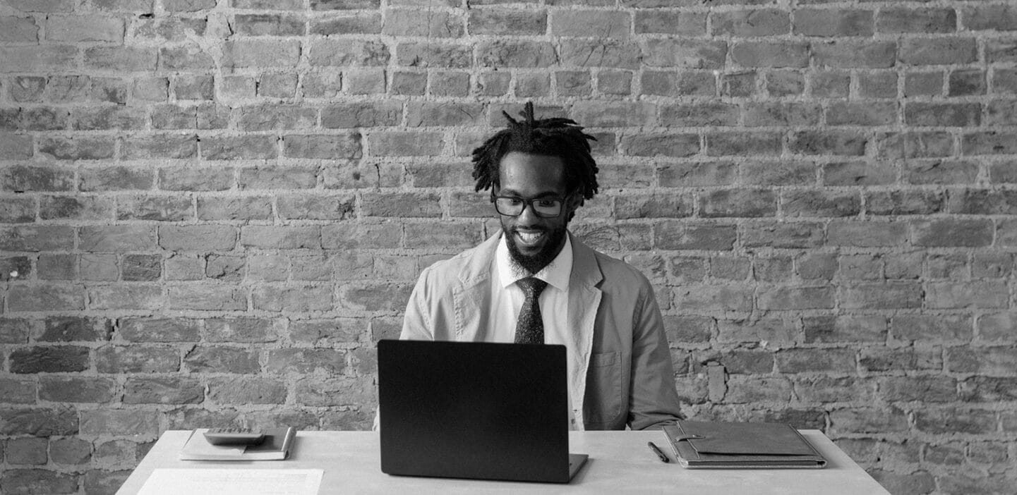 Man seated at a laptop in front of a brick wall