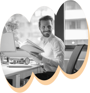 Smiling man in a white shirt looking up from a book at his modern office desk.