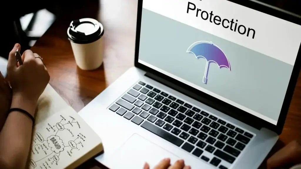 Liable insurance definition represented by two people taking notes sit at a laptop displaying an umbrella with the word 'protection' over it